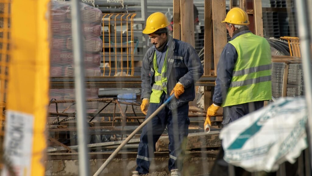 Two construction workers in safety gear collaborate efficiently in a busy construction site, emphasizing teamwork and hard work.