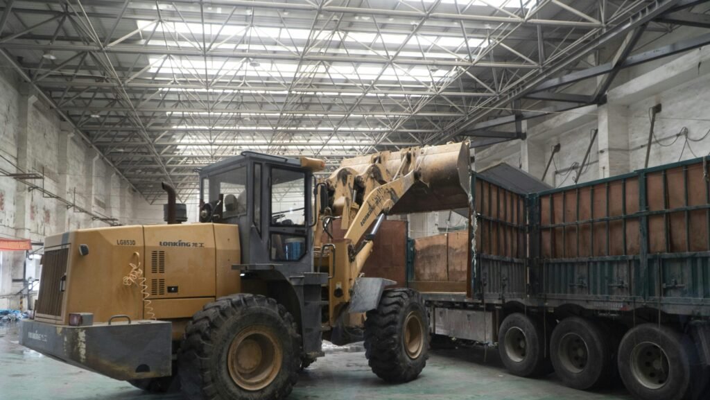 Heavy-duty loader transferring materials onto a truck inside a large warehouse.